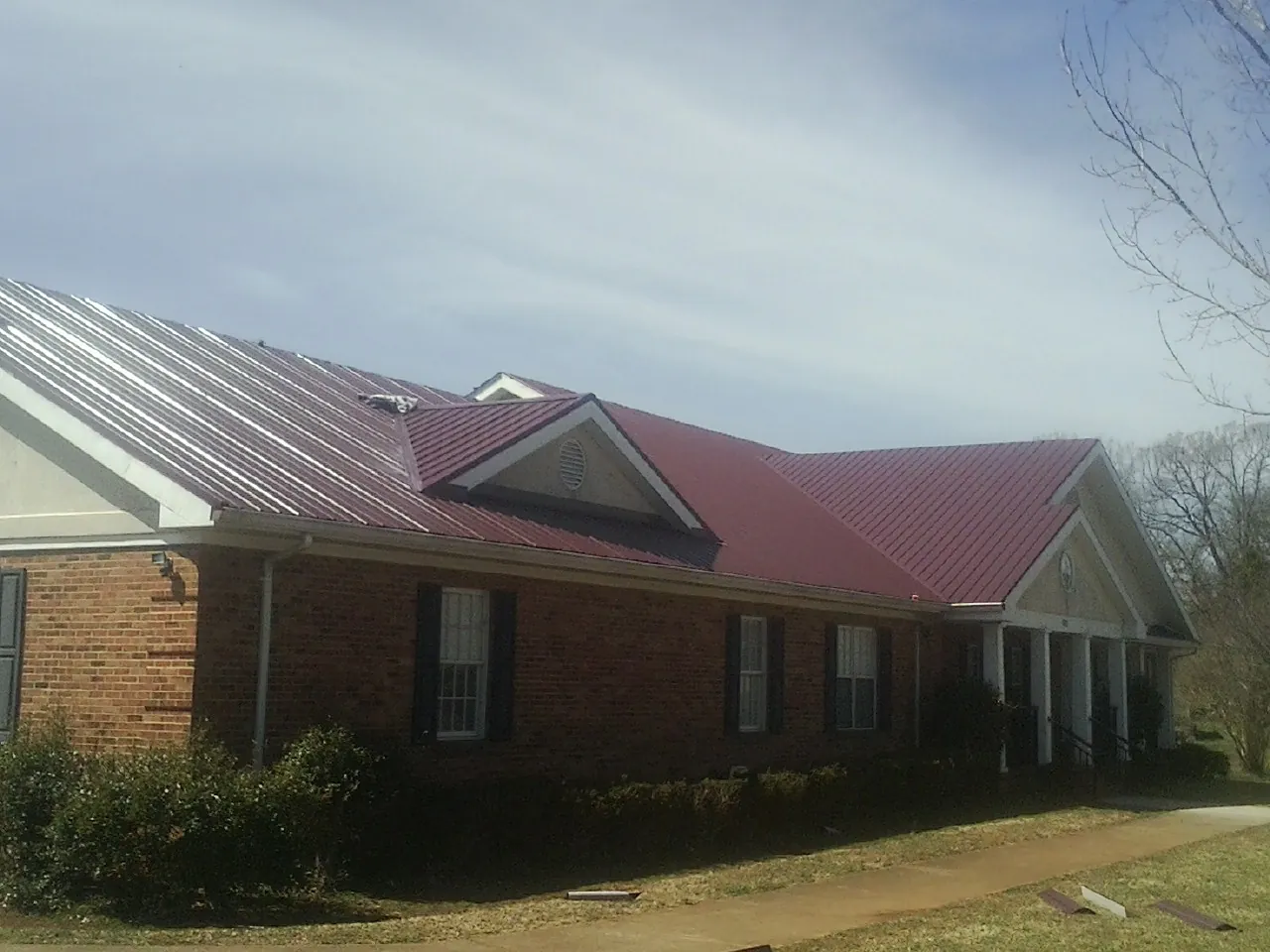 Red metal roof with gabled entries on a long brick building, from a Hail Damage Roof Repair job in Crown Point
