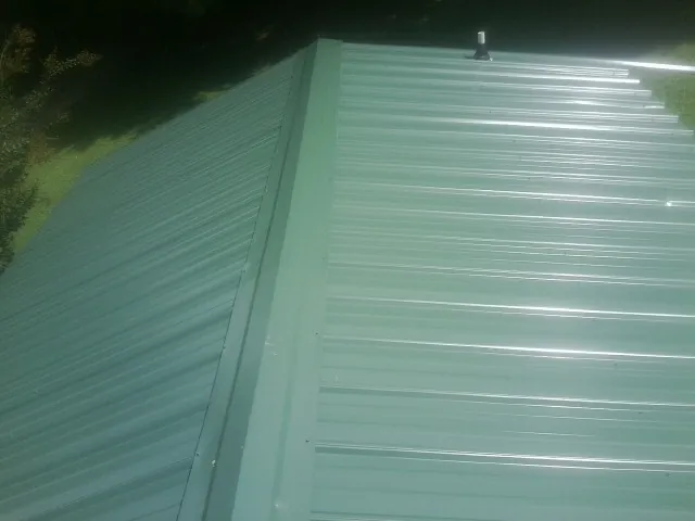 New green metal panels meeting at the ridge of a roof — Flat Roof Repair work by our crew in Crown Point