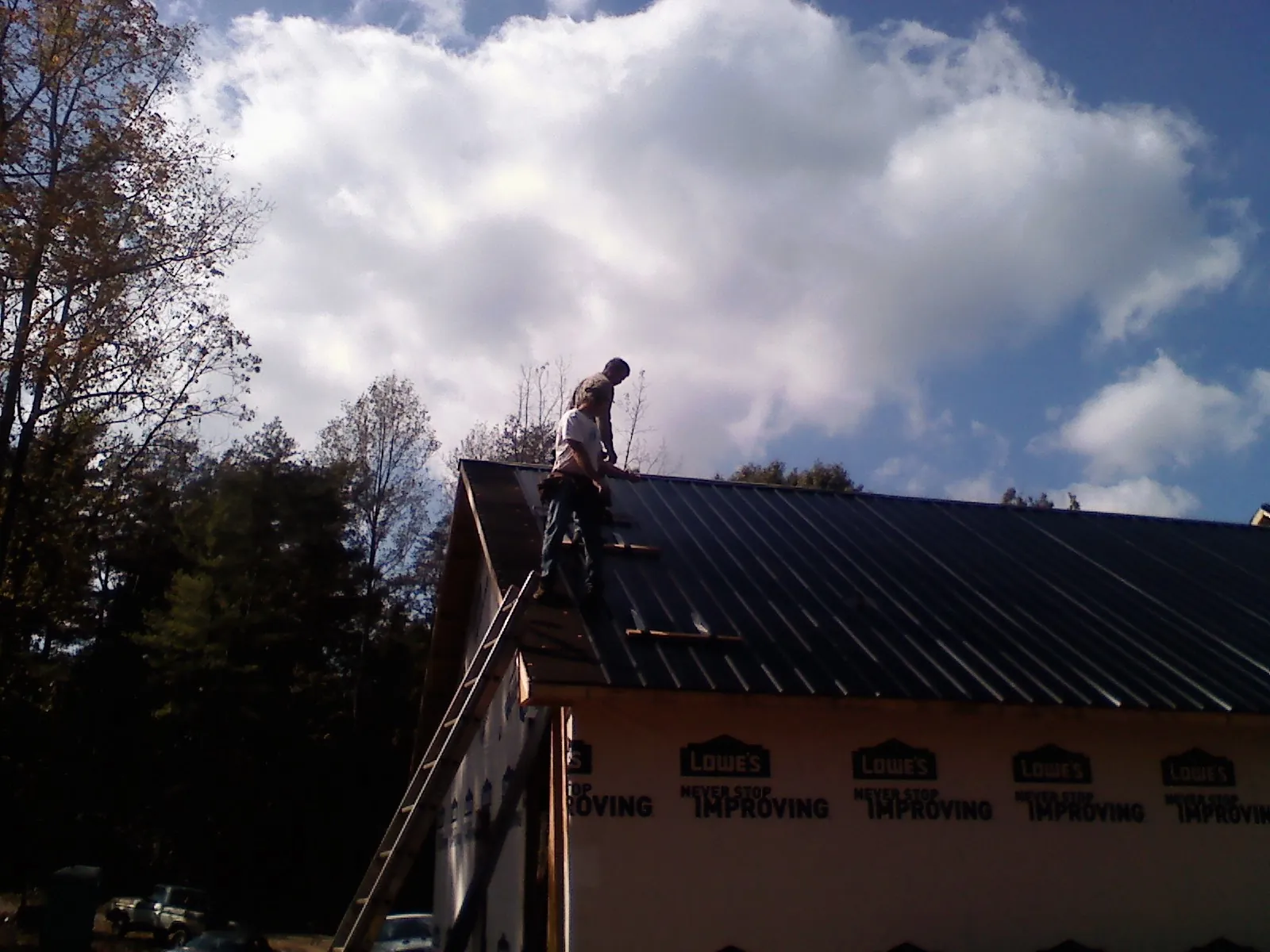 Roofer fastening dark metal panels high against a cloudy sky, from a Roof Inspection job in Crown Point